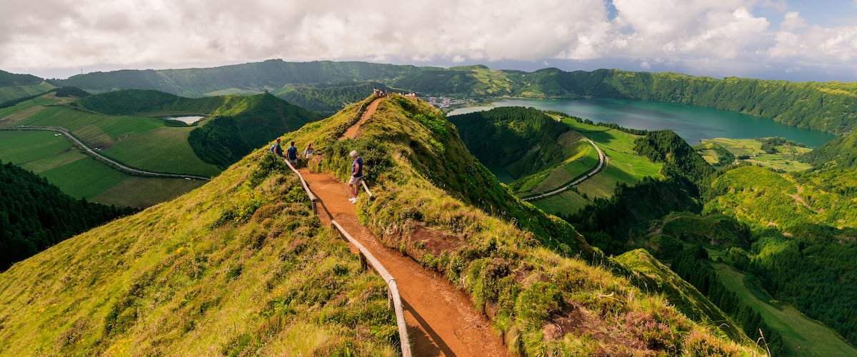 A hiking trail on a grassy hill with a view of a lake and surrounding hills.