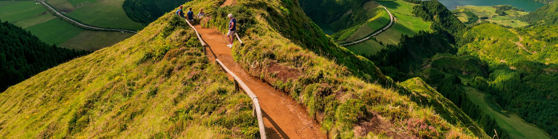 A hiking trail on a grassy hill with a view of a lake and surrounding hills.