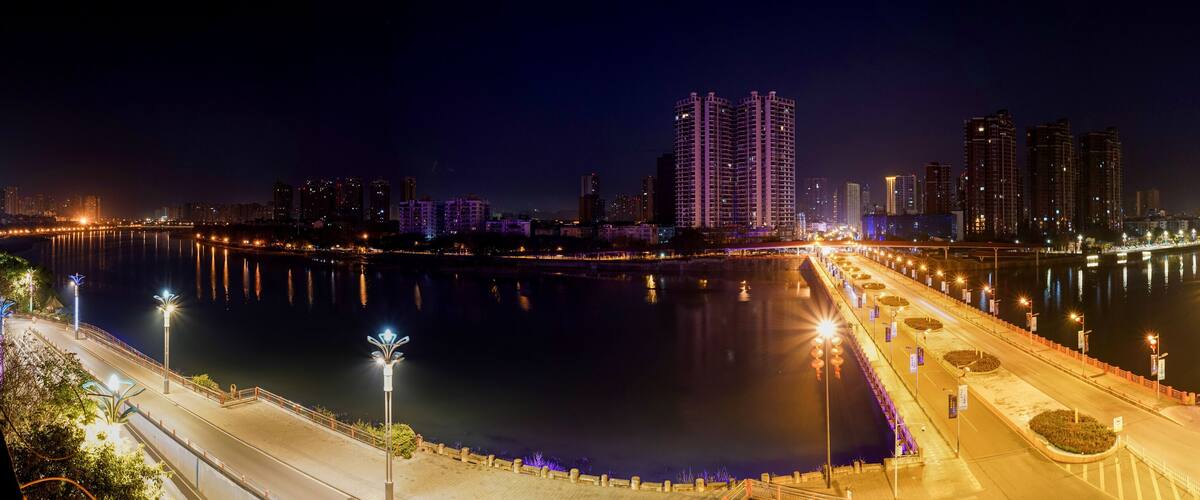 A nighttime cityscape with a river, illuminated buildings, and a bridge.