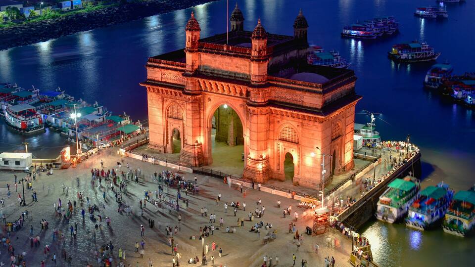 A large illuminated building with two towers, surrounded by a busy waterfront with boats and people.