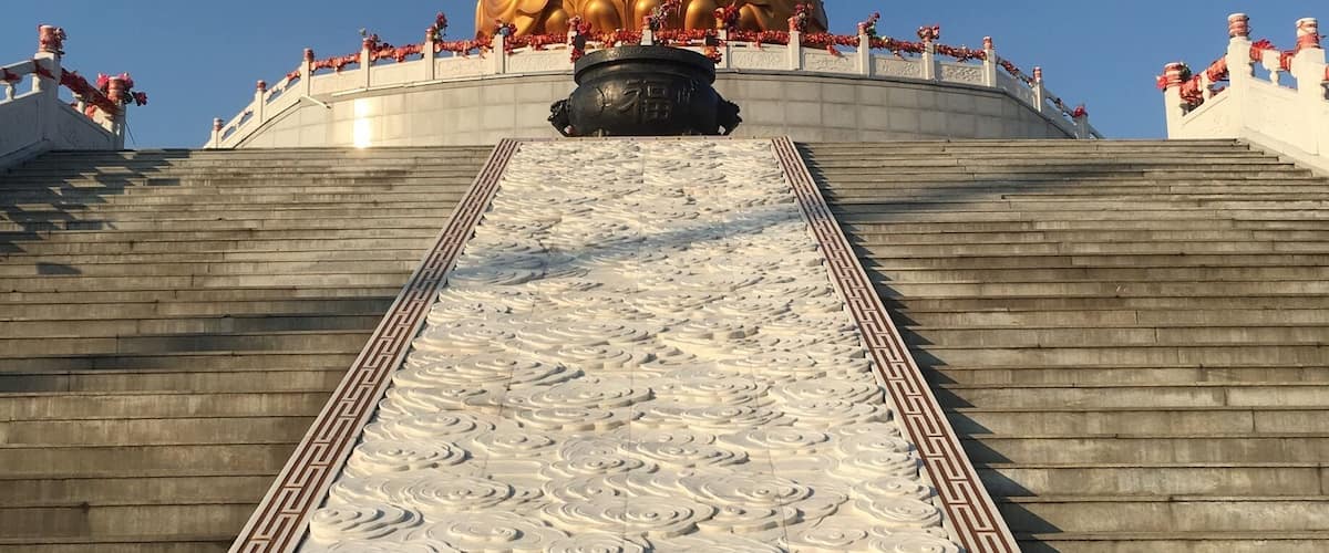 A large golden Buddha statue on a platform with intricate carvings, surrounded by a railing and red decorations.