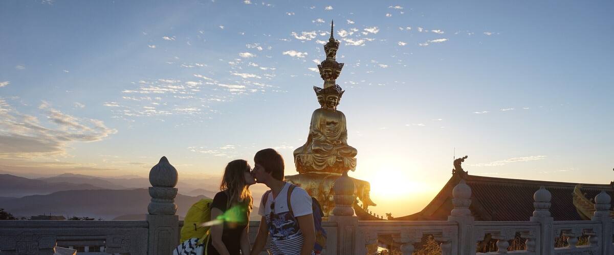 Una pareja besándose frente a una gran estatua dorada al atardecer.