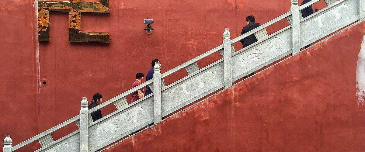 A red wall with a large gold Chinese character and a staircase.