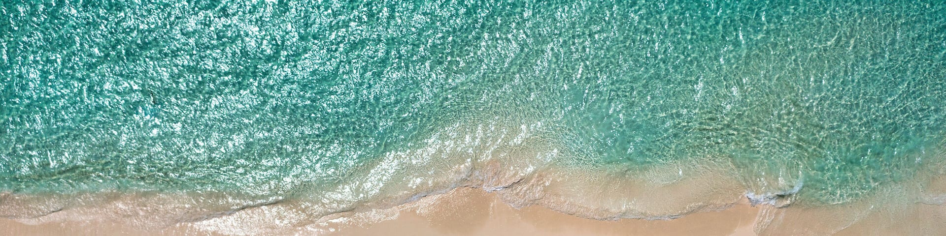 An aerial view of a beach with turquoise water, a sandy shore, and colorful umbrellas lined up along the beach.