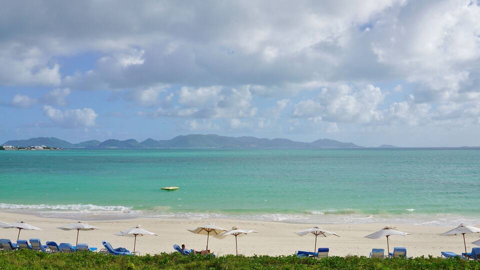 A beach with turquoise water, white sand, and blue sky with clouds.