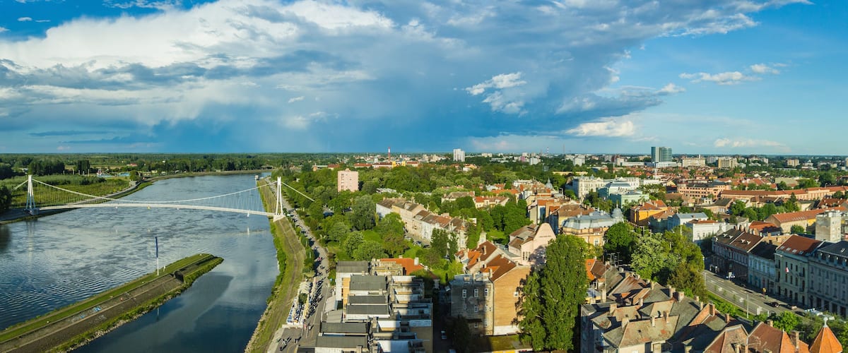 A river with a bridge, a cityscape with historic buildings, and a cloudy sky.