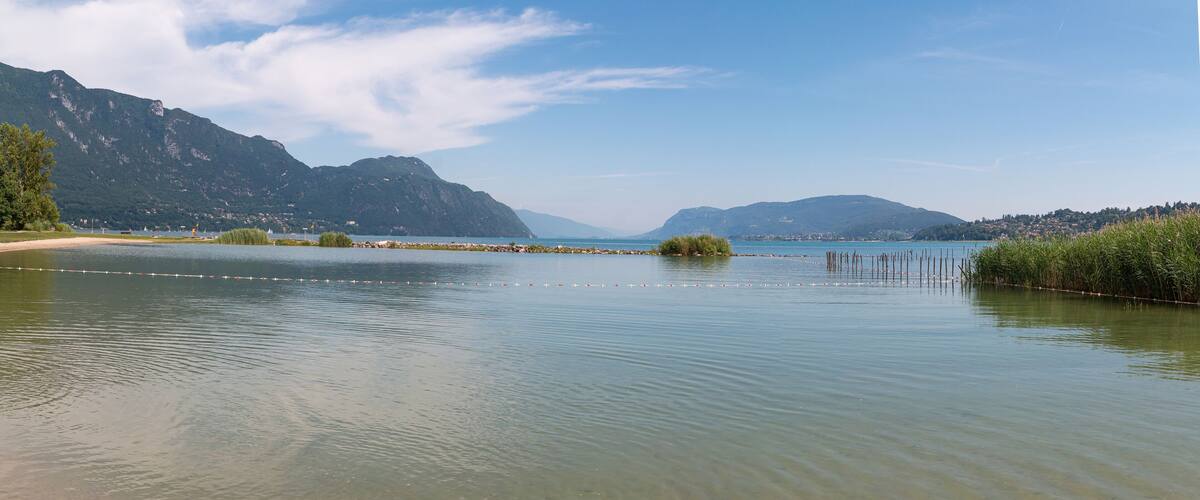 A calm lake with clear water, surrounded by mountains and a distant town.