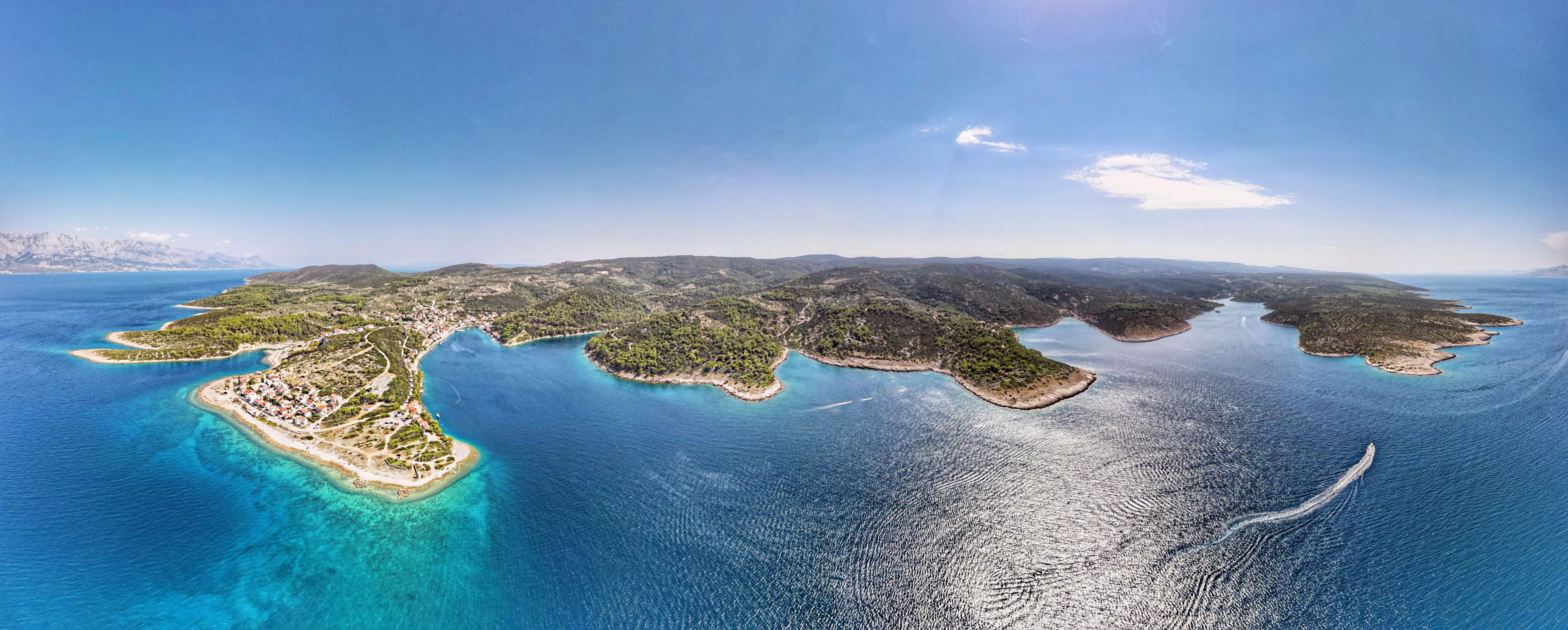 Vista aérea de un paisaje costero con una isla grande rodeada de aguas azules cristalinas, mostrando una mezcla de vegetación verde y playas de arena.