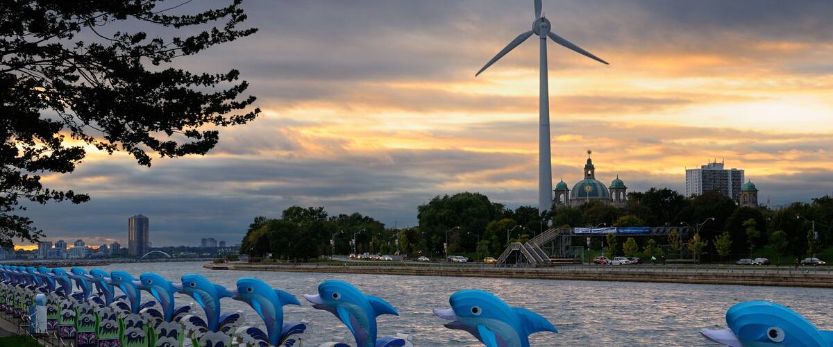A river with a wind turbine and a row of dolphin sculptures along the riverbank.