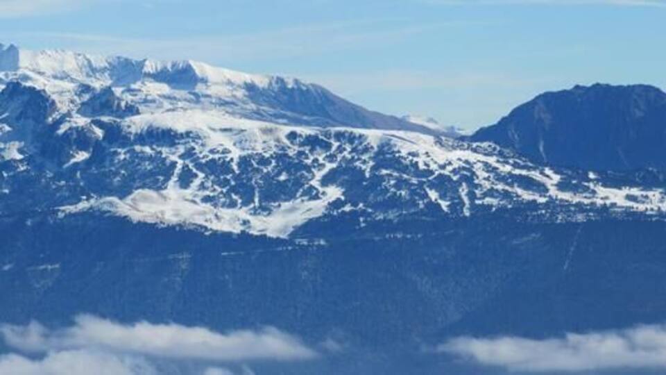 A snow-covered mountain range with a clear sky and clouds below.