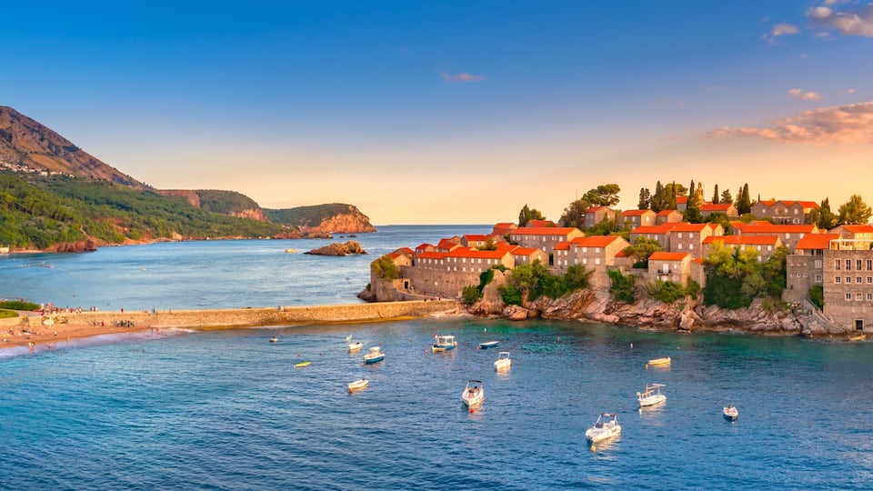 A coastal town with a castle on a cliff, a beach, and boats in the water.