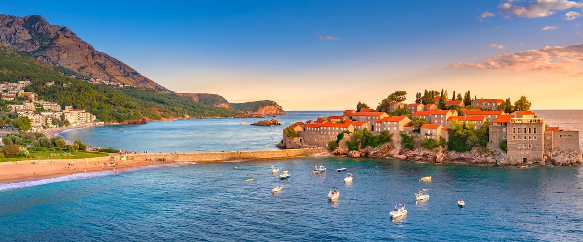 A coastal town with a castle on a cliff, a beach, and boats in the water.