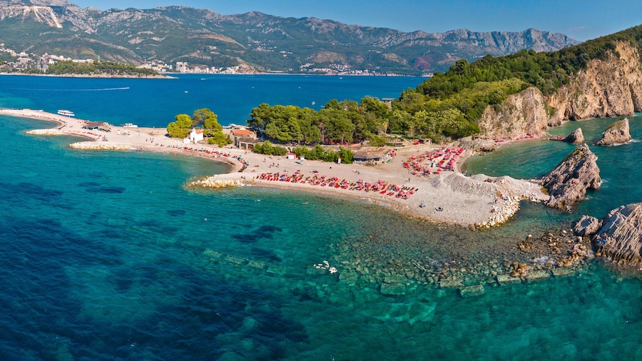 Aerial view of Sveti Nicola, Budva island, Montenegro. Hawaii beach, umbrellas and bathers and crystal clear waters. Jagged coasts with sheer cliffs overlooking the transparent sea. Wild nature
