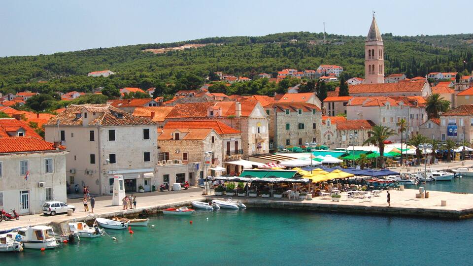 A coastal town with red-roofed buildings, a church tower, and a marina with boats.