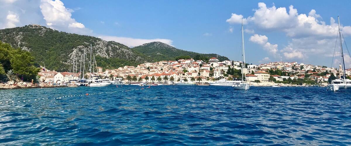 A coastal town with boats, a clear sky, and mountains in the background.