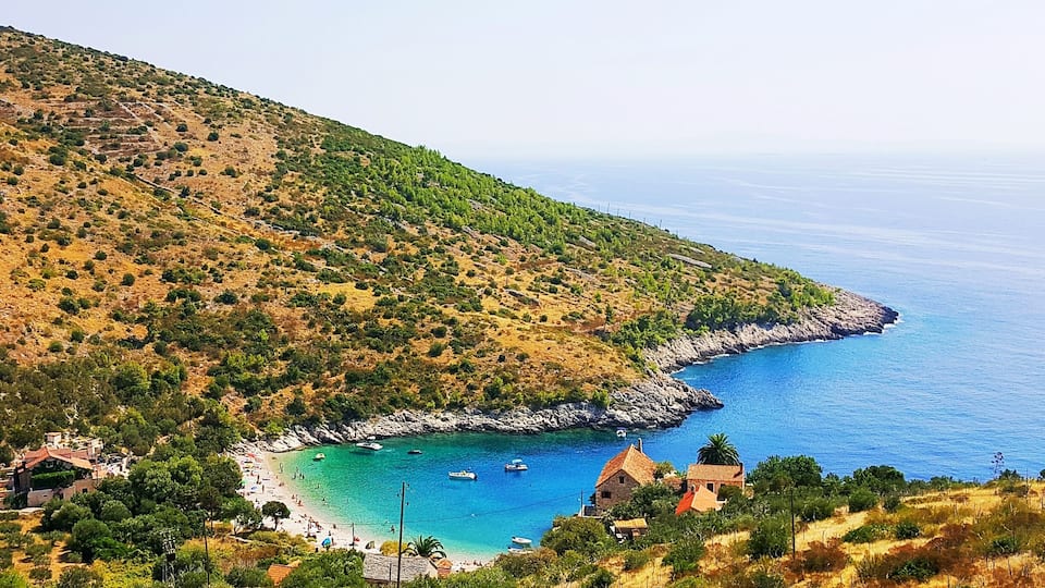 A coastal landscape with a beach, boats, and buildings.
