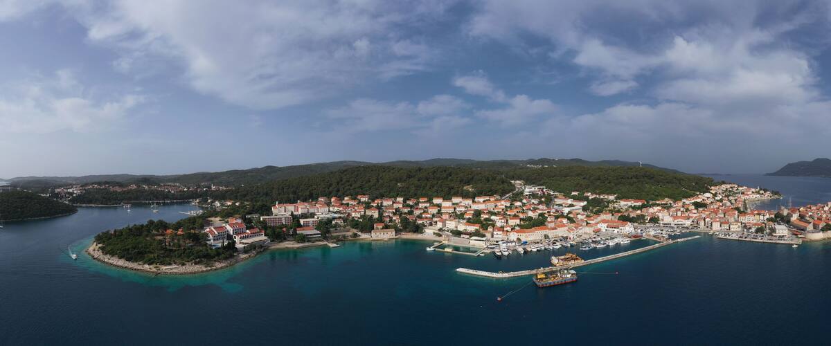 An aerial view of a coastal town with a marina, surrounded by hills and clear blue waters.