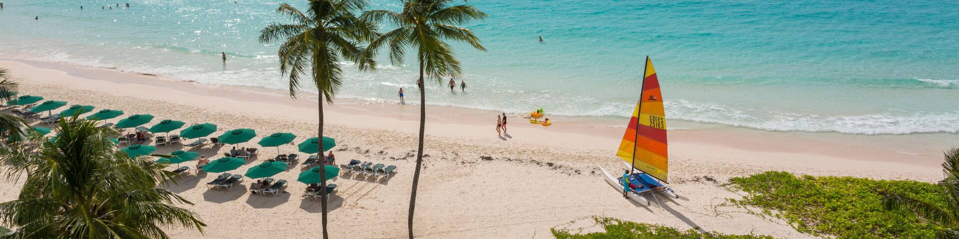 A beach with turquoise water, palm trees, and a sailboat.
