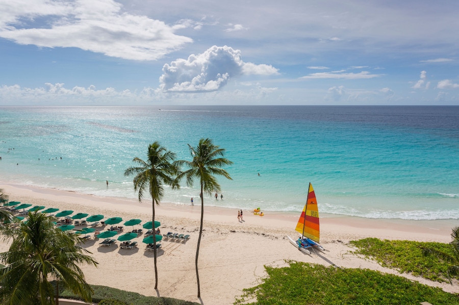 A beach with turquoise water, palm trees, and a sailboat.