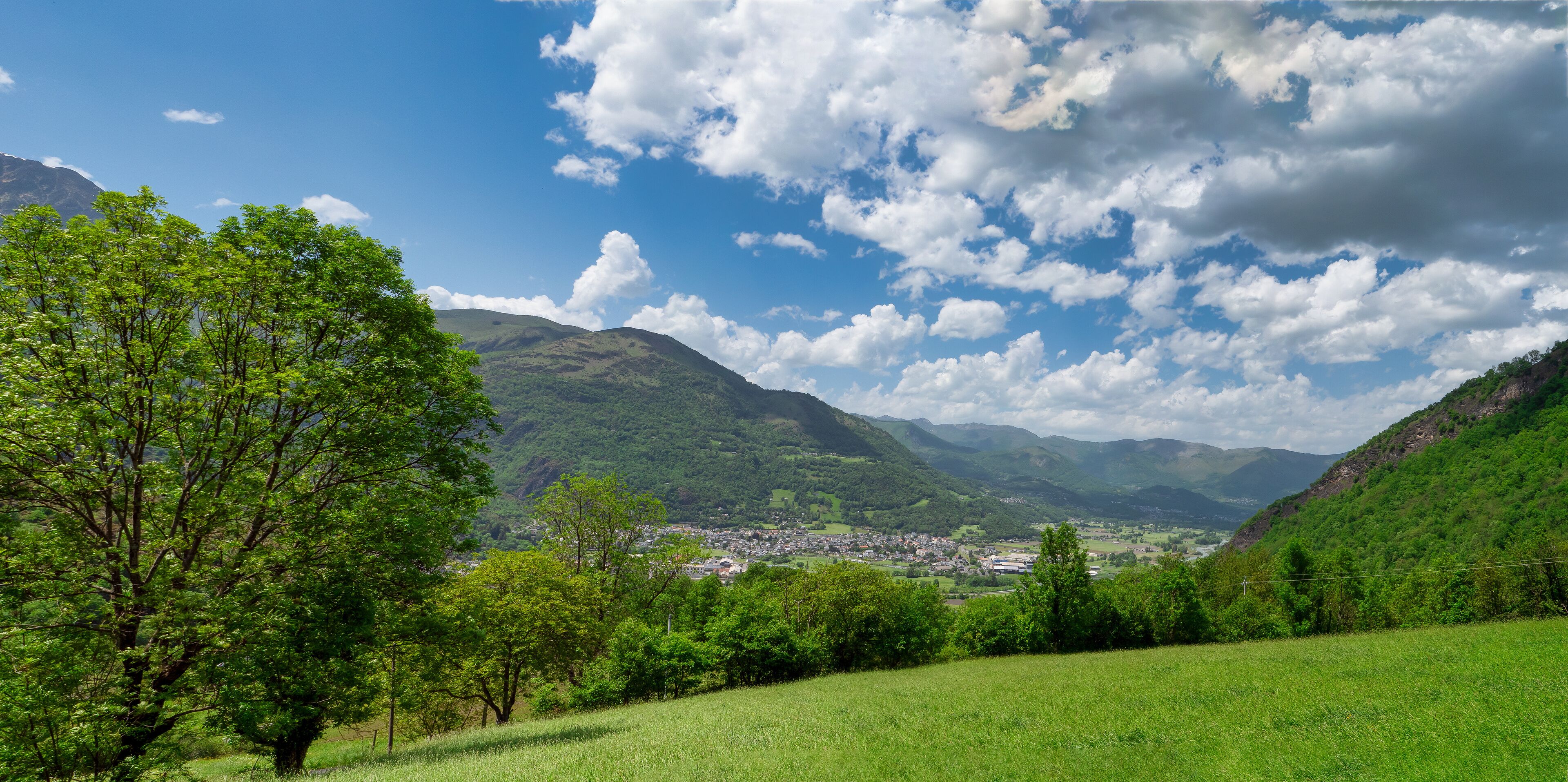 A valley with a town, green hills, and a mountain in the background.