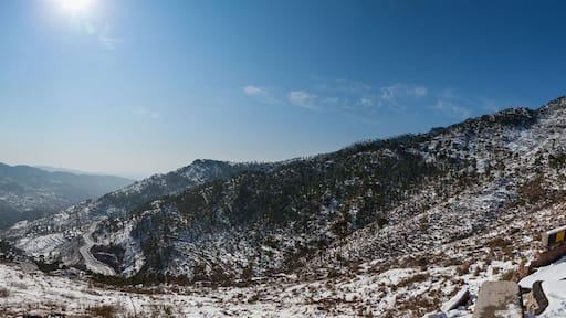 View of snow-dusted mountains and winding roads under a bright sun, a serene winter landscape in Murree, Punjab, Pakistan.