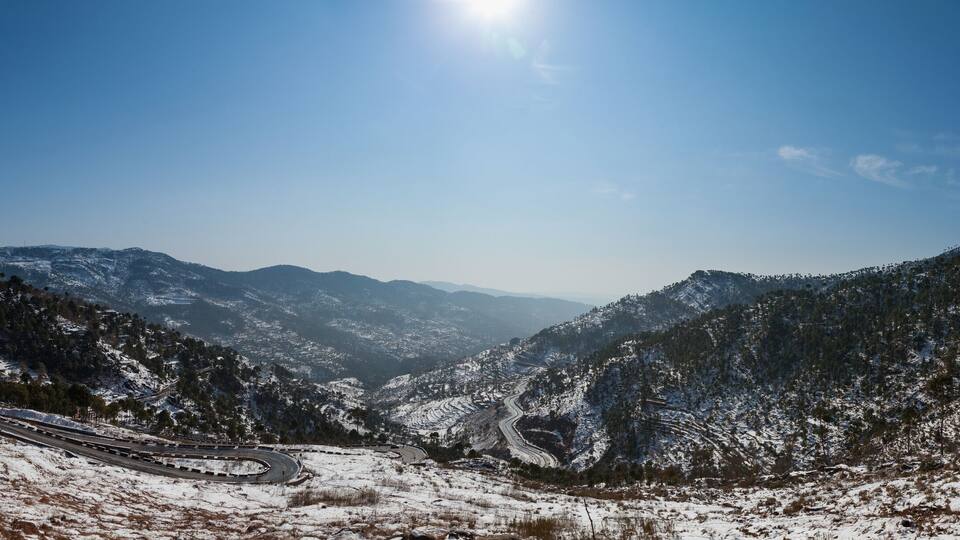 A snow-covered mountainous landscape with winding roads and a clear blue sky.