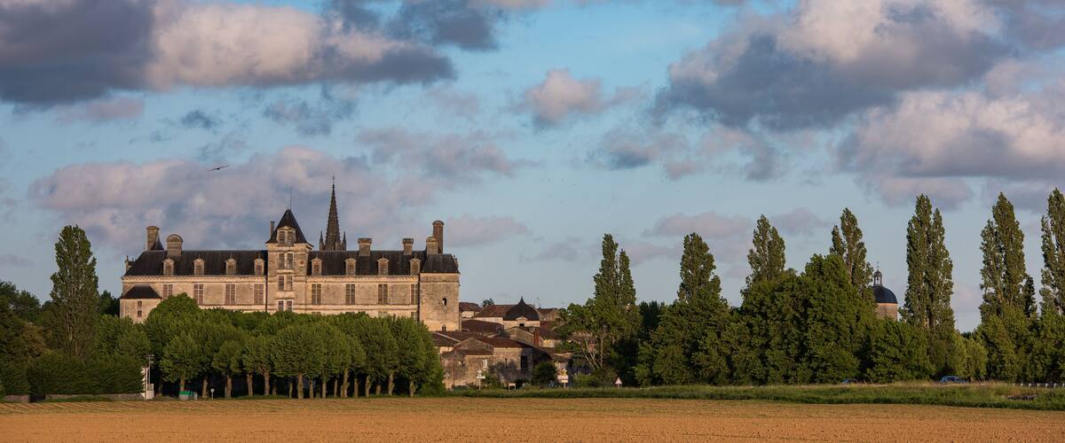 A historic building with a spire, surrounded by trees and fields.