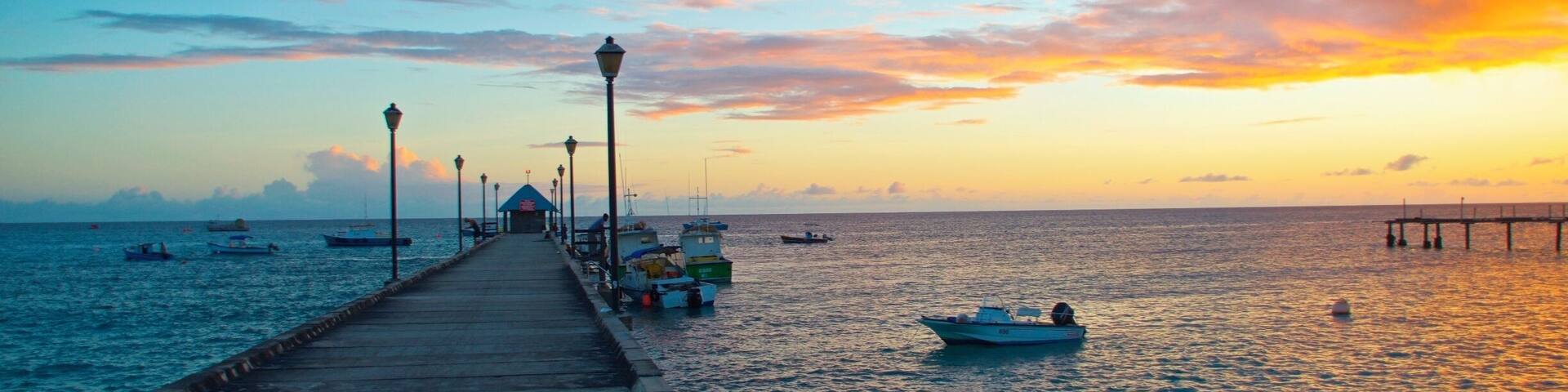 A pier extending into calm waters at sunset with boats docked and a colorful sky.