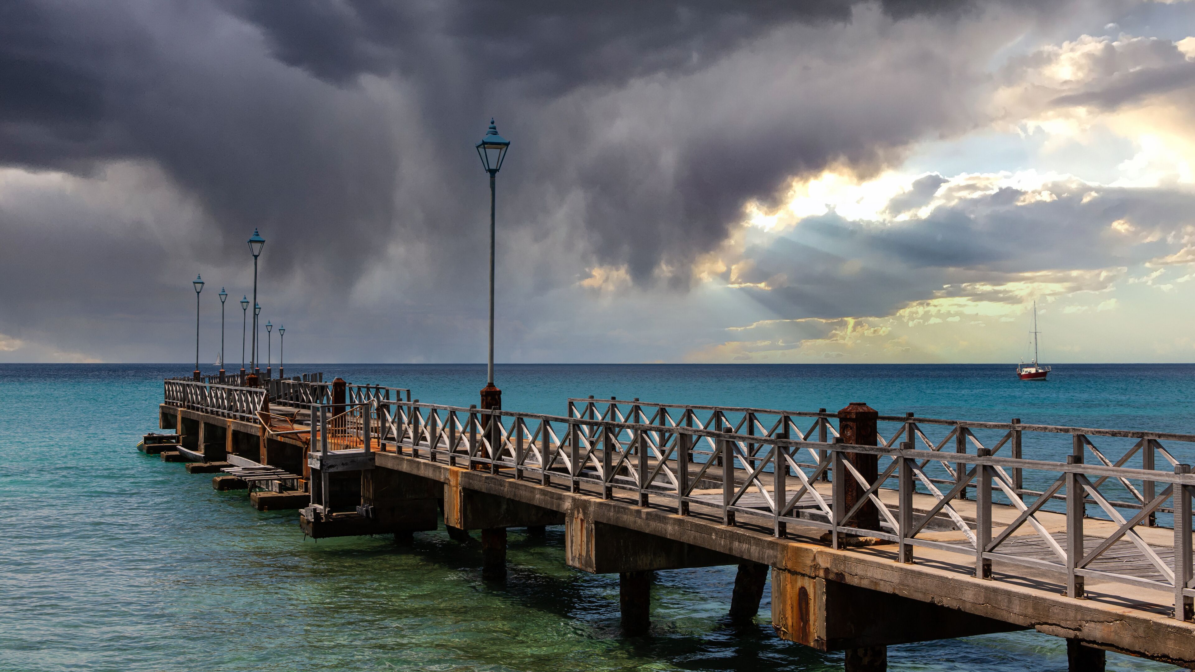 A pier extending into the ocean with a sailboat in the distance.