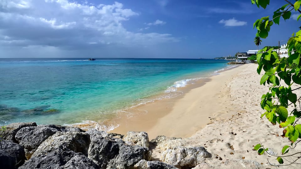 A beach with clear turquoise water, a sandy shore, and a rocky foreground.
