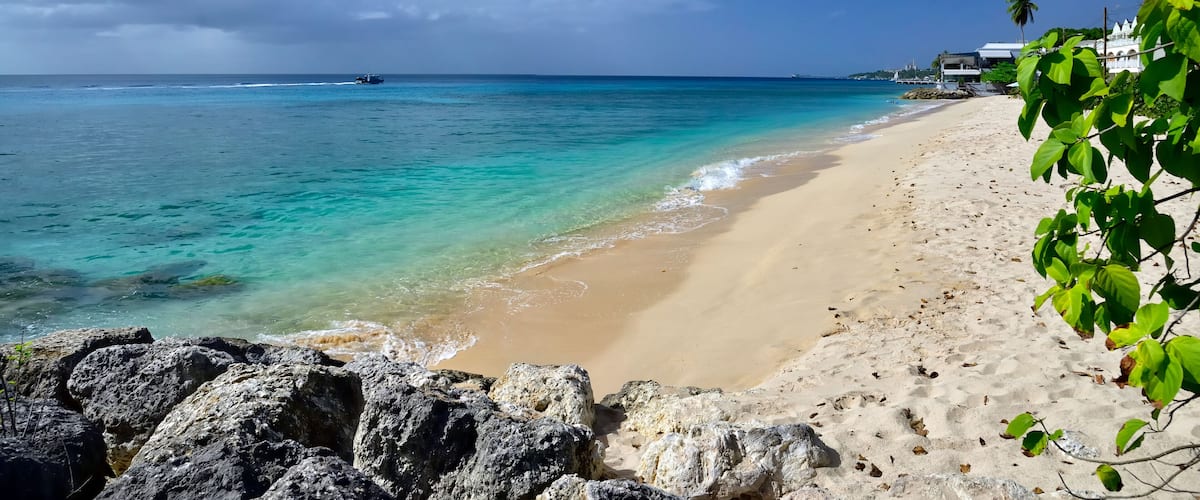 A beach with clear turquoise water, a sandy shore, and a rocky foreground.
