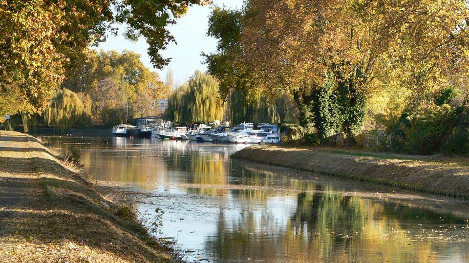 A canal lined with trees reflecting boats and a path.