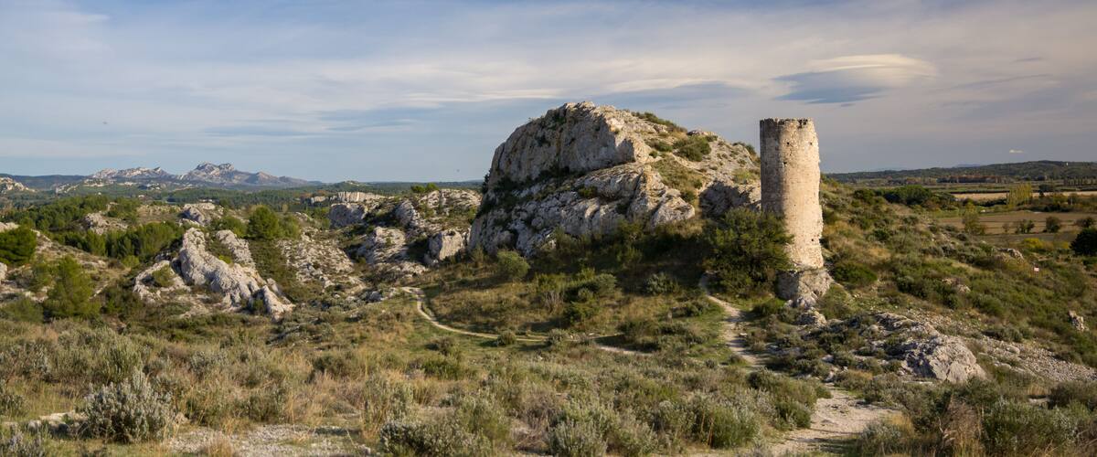 A rugged landscape with a prominent rocky hill and a tall, narrow tower.