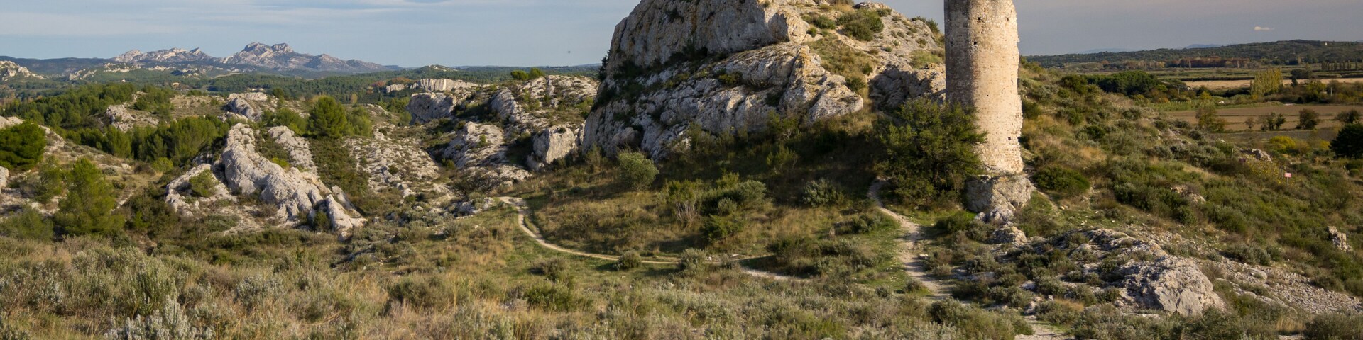 A rugged landscape with a prominent rocky hill and a tall, narrow tower.