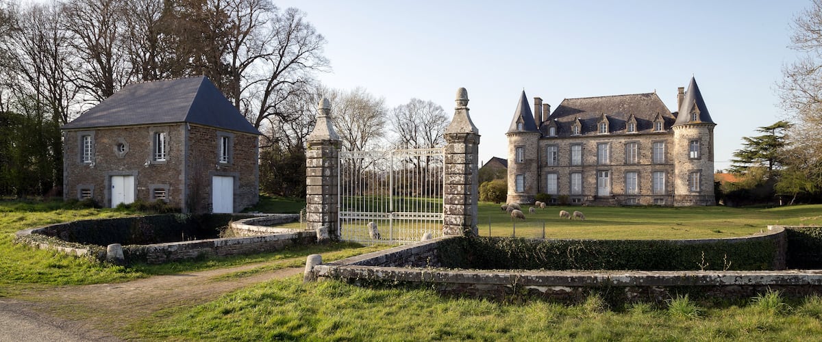 A historic stone building with a small annex and a large estate with multiple towers and a well-maintained lawn.