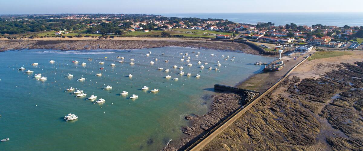 A coastal town with a harbor filled with boats, a rocky shoreline, and residential buildings in the background.