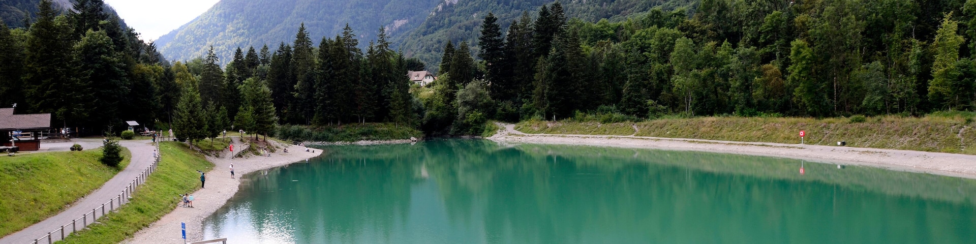 Un lago rodeado de montañas, un muelle de madera y un sendero.