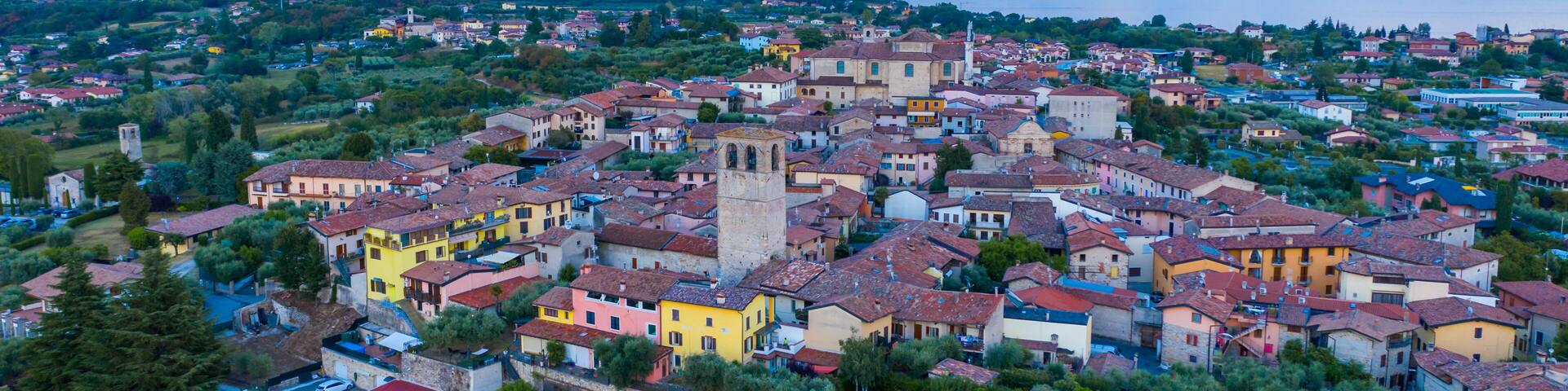 Aerial view of village near Lago di Garda Italy. Beautiful sunset light. Flying close to the church tower revealing Lago di Garda on the horizon. Manerba del Garda town in Brescia Italy.