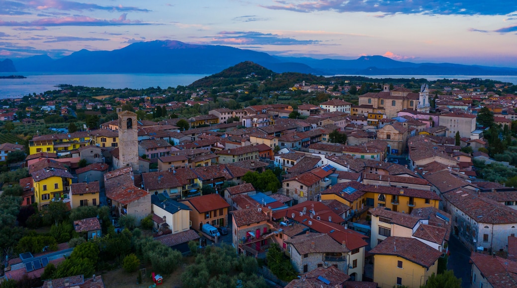 Aerial view of village near Lago di Garda Italy. Beautiful sunset light. Flying close to the church tower revealing Lago di Garda on the horizon. Manerba del Garda town in Brescia Italy.