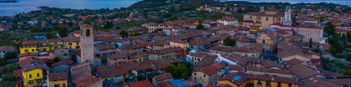 Aerial view of village near Lago di Garda Italy. Beautiful sunset light. Flying close to the church tower revealing Lago di Garda on the horizon. Manerba del Garda town in Brescia Italy.