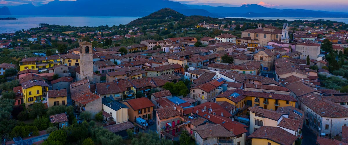 Aerial view of village near Lago di Garda Italy. Beautiful sunset light. Flying close to the church tower revealing Lago di Garda on the horizon. Manerba del Garda town in Brescia Italy.