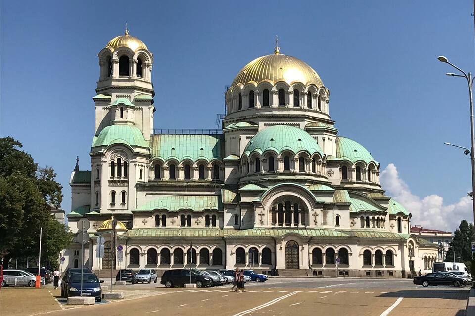 Een grote kathedraal met meerdere koepels en torens, een opvallende gouden koepel en groene dakbedekking.