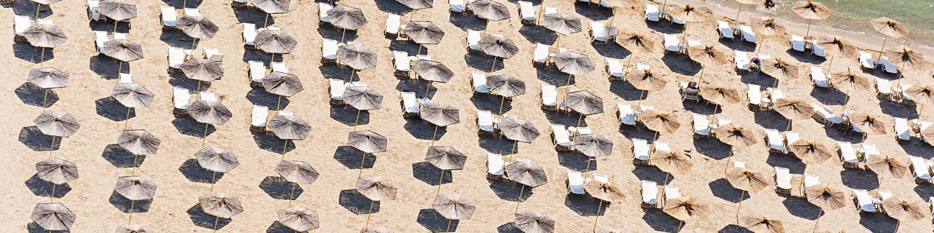 A beach with numerous hexagonal umbrellas and white lounge chairs arranged in rows.