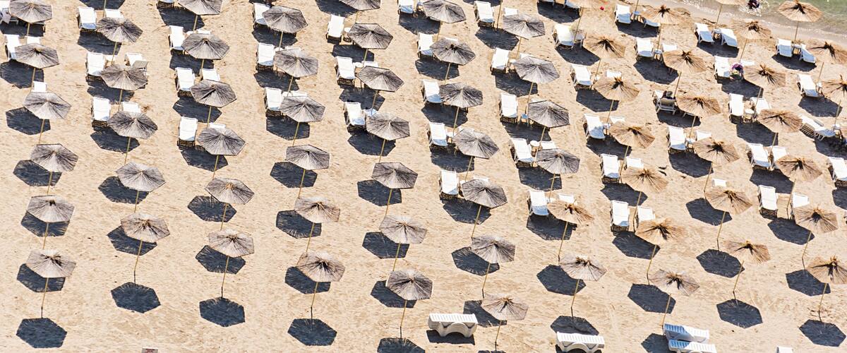 A beach with rows of hexagonal umbrellas and white lounge chairs.