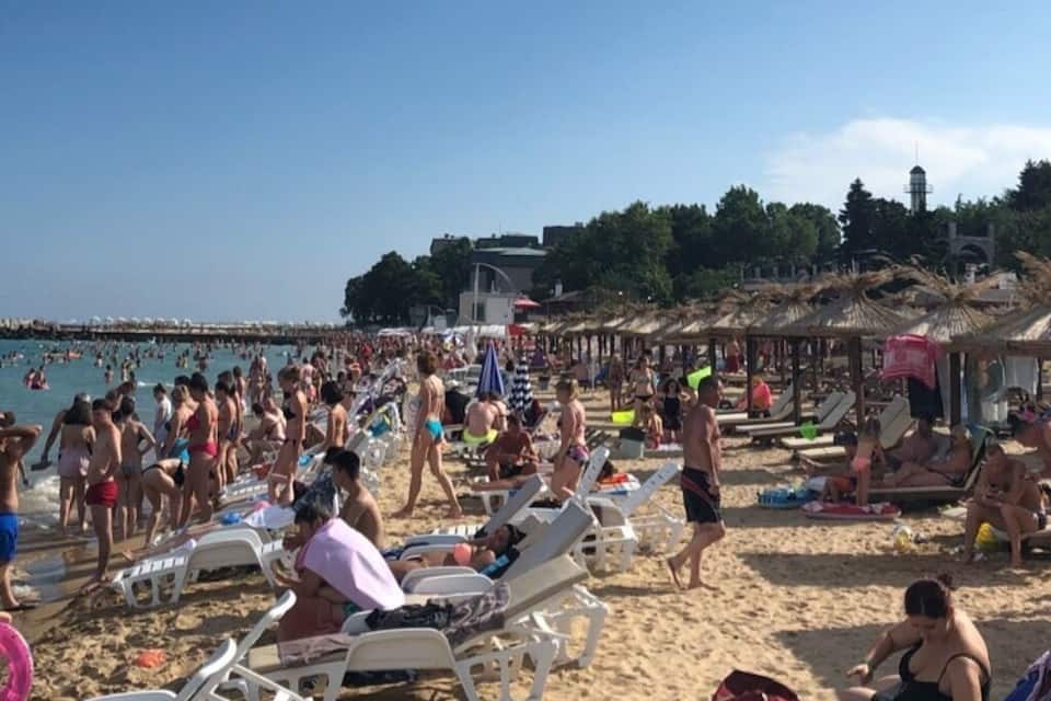 A crowded beach with people sunbathing and swimming.
