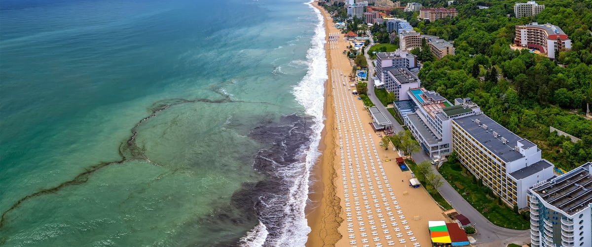 A coastal cityscape with a beach, hotel buildings, and a hilly backdrop.