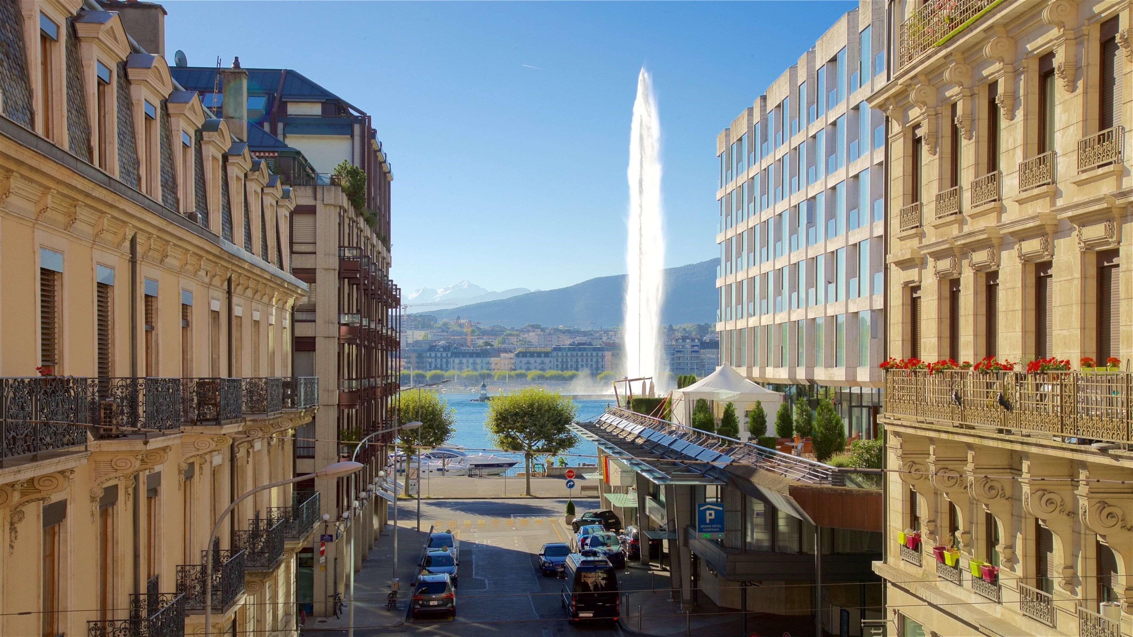 A city street with historic buildings, a fountain, and a mountain in the background.