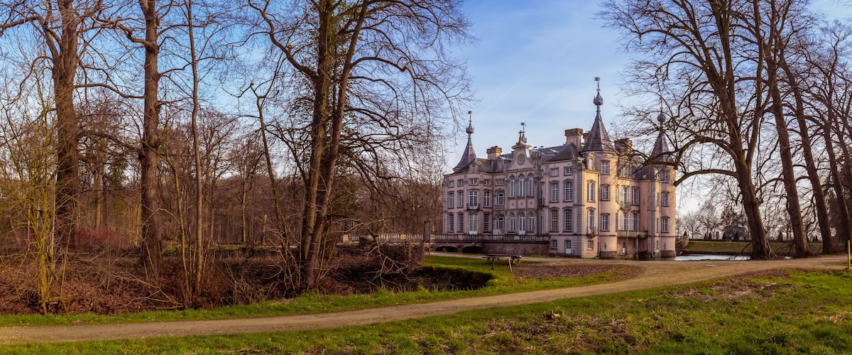 A historic building with multiple towers, surrounded by a park with a pathway and leafless trees.