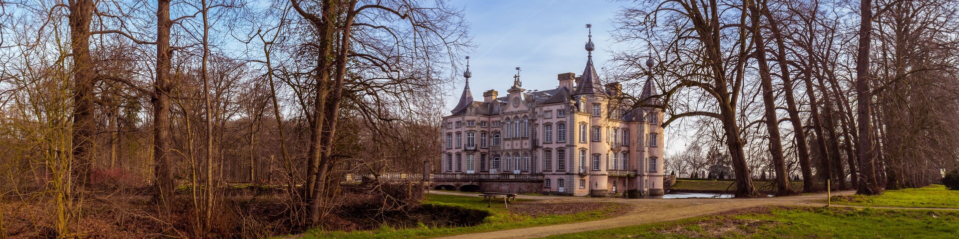 A historic building with multiple towers, surrounded by a park with a pathway and leafless trees.