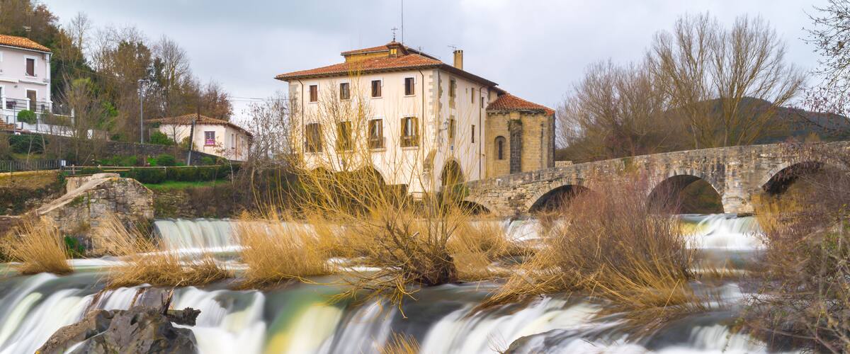 A waterfall with a stone bridge and a building in the background.